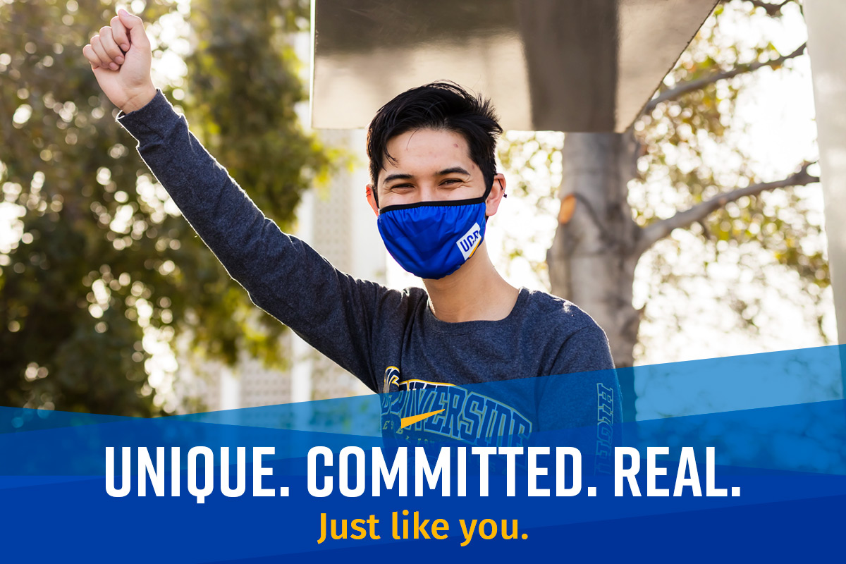A student celebrates the UCR student experience on campus while wearing university gear and a face mask.