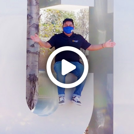 Video play button over a male student wearing a protective face mask and is sitting on the C of the UCR sculpture on the university campus