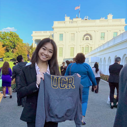 Catherine Mah holds up a UCR sweatshirt in front of a government building.