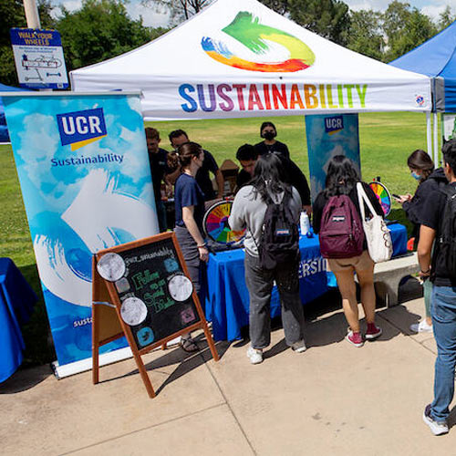 A sustainability tabling event is being conducted on campus. There is a tent with the word "sustainability" printed on the front panel.