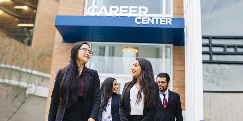 Four students walk out of the Career center in professional attire.